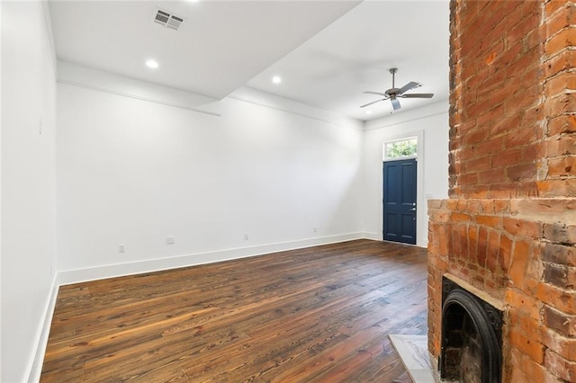 unfurnished living room with a brick fireplace, dark wood-type flooring, and ceiling fan