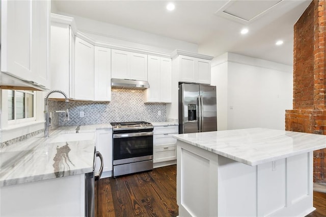 kitchen with appliances with stainless steel finishes, dark hardwood / wood-style flooring, a kitchen island, light stone countertops, and white cabinets