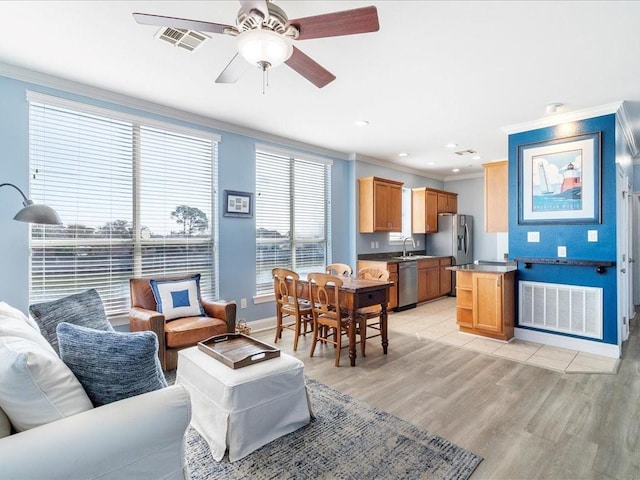 living room with ornamental molding, visible vents, light wood-style floors, and ceiling fan