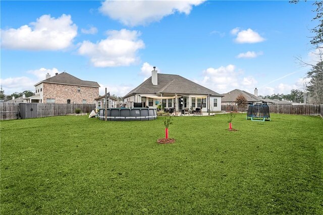 back of house with a fenced in pool, a trampoline, and a lawn