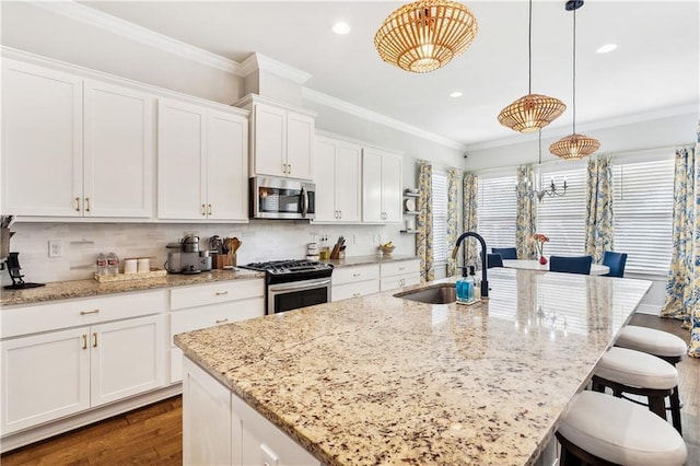 kitchen featuring pendant lighting, crown molding, appliances with stainless steel finishes, white cabinetry, and an island with sink