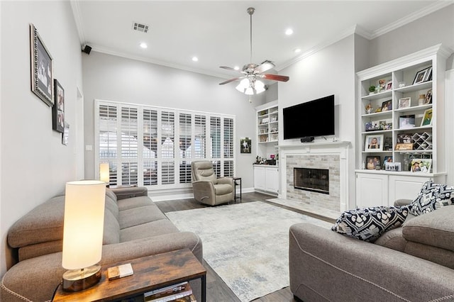 living room with a tile fireplace, hardwood / wood-style floors, a high ceiling, ceiling fan, and crown molding