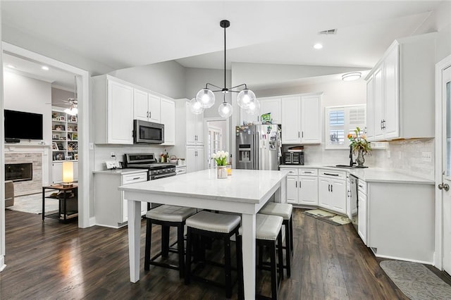 kitchen featuring a kitchen bar, white cabinetry, a tile fireplace, a kitchen island, and stainless steel appliances