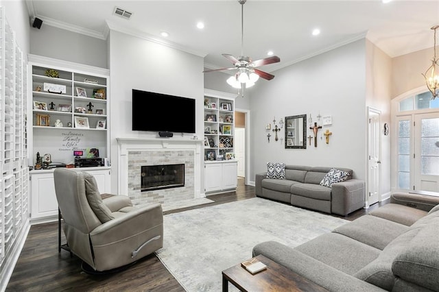 living room with dark hardwood / wood-style floors, ceiling fan with notable chandelier, a tiled fireplace, ornamental molding, and a high ceiling