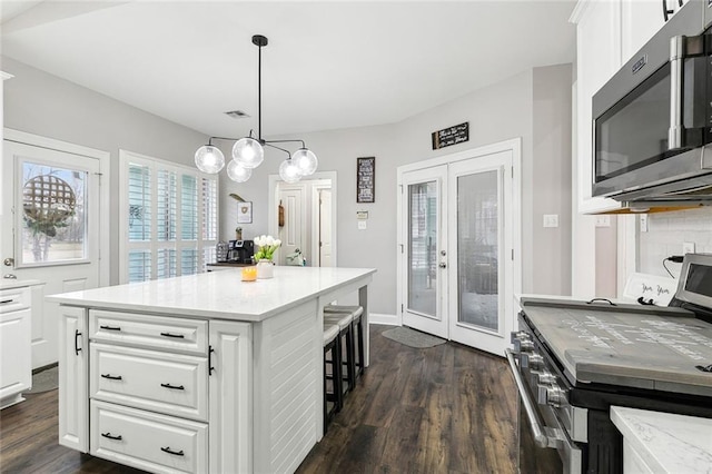 kitchen featuring dark wood-type flooring, stainless steel appliances, white cabinets, a kitchen island, and decorative light fixtures