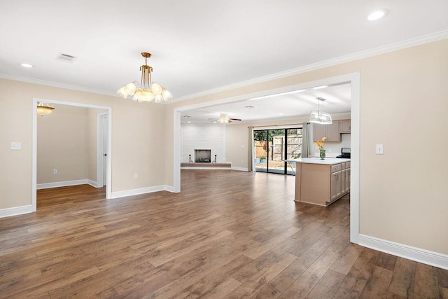 unfurnished living room featuring ceiling fan with notable chandelier, wood-type flooring, ornamental molding, and a large fireplace