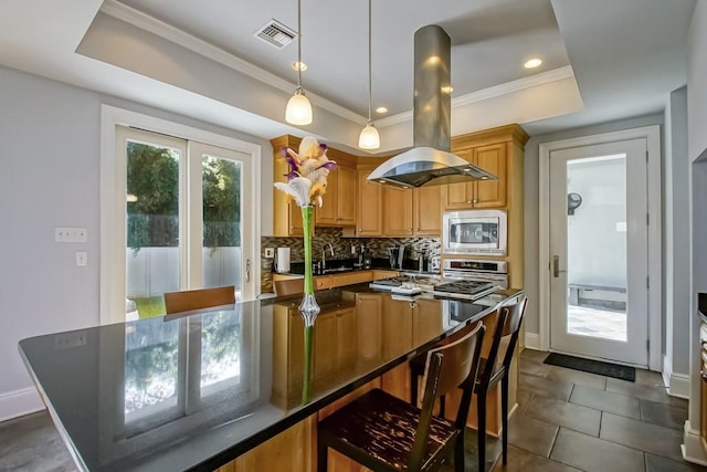 kitchen with pendant lighting, backsplash, stainless steel microwave, island range hood, and a raised ceiling