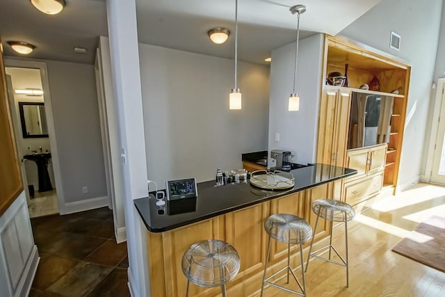 kitchen featuring dark wood-type flooring, a kitchen bar, kitchen peninsula, and hanging light fixtures