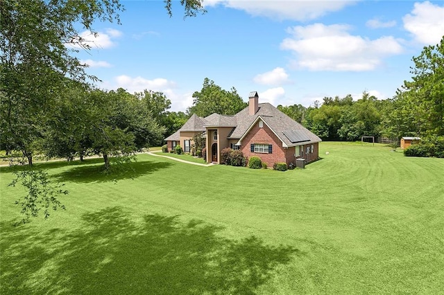 rear view of property featuring solar panels, a chimney, and a lawn