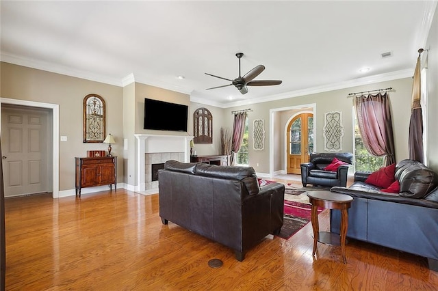 living room featuring crown molding, light wood finished floors, a ceiling fan, a tile fireplace, and baseboards