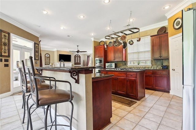 kitchen featuring a breakfast bar area, appliances with stainless steel finishes, dark brown cabinets, and ornamental molding