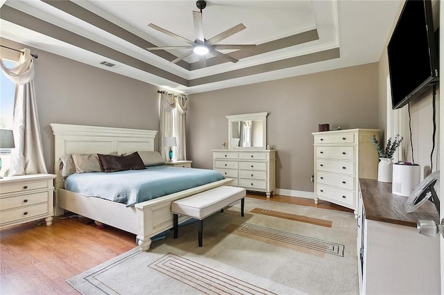 bedroom with light wood-style flooring, visible vents, a raised ceiling, and crown molding