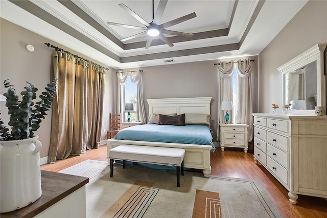 bedroom with a raised ceiling, visible vents, crown molding, and wood finished floors