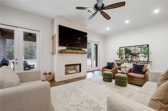 living room with crown molding, ceiling fan, hardwood / wood-style floors, a large fireplace, and french doors