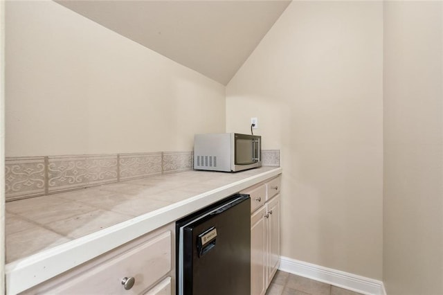 kitchen with lofted ceiling, tile counters, refrigerator, and light tile patterned floors