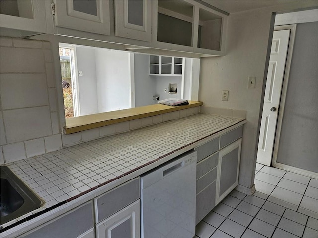 kitchen with light tile patterned flooring, sink, white cabinetry, tile countertops, and dishwasher