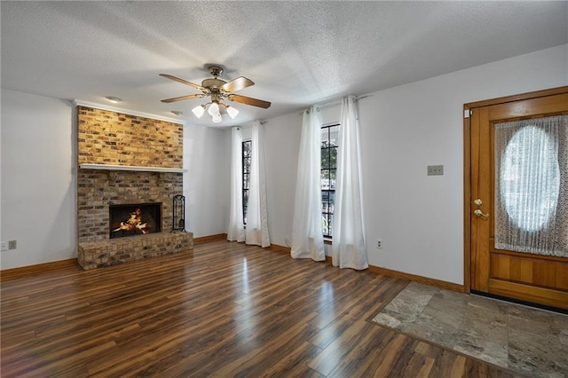 unfurnished living room featuring ceiling fan, a fireplace, dark hardwood / wood-style floors, and a textured ceiling