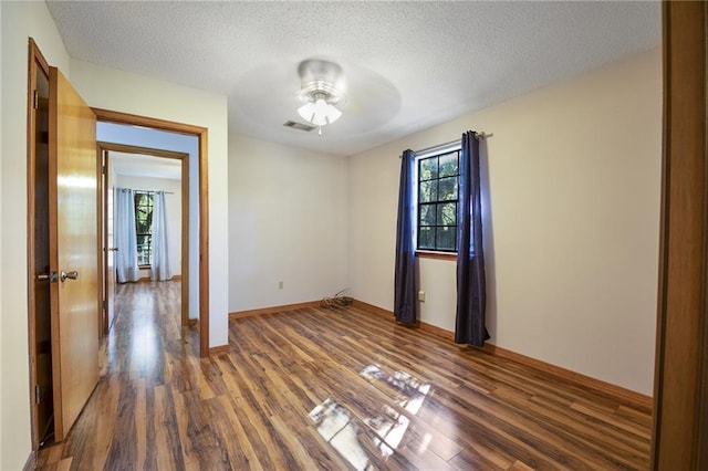 empty room with dark wood-type flooring, a healthy amount of sunlight, and a textured ceiling