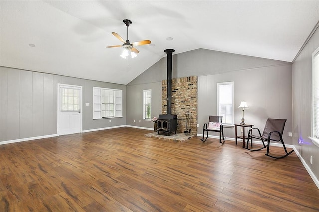 unfurnished room with dark wood-type flooring, a ceiling fan, baseboards, vaulted ceiling, and a wood stove