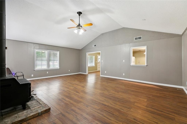 unfurnished living room with lofted ceiling, wood finished floors, visible vents, a ceiling fan, and a wood stove