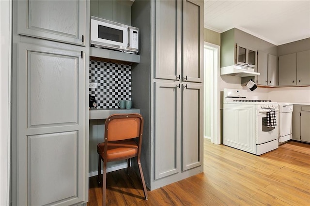 kitchen featuring white appliances, light wood-style flooring, crown molding, under cabinet range hood, and built in desk