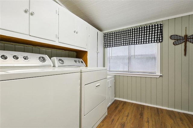 clothes washing area featuring dark wood-style flooring, cabinet space, washing machine and dryer, wooden walls, and baseboards