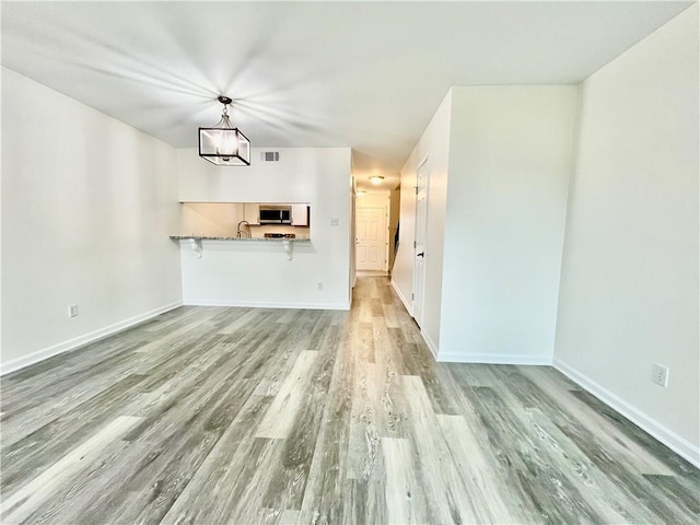 unfurnished living room featuring sink, a notable chandelier, and light wood-type flooring