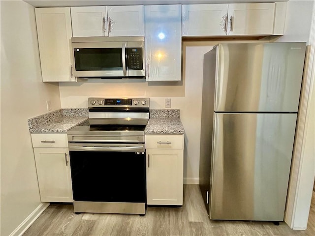 kitchen with light stone counters, stainless steel appliances, white cabinets, and light wood-type flooring