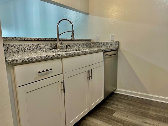 kitchen featuring dark hardwood / wood-style floors, white cabinetry, sink, stainless steel dishwasher, and light stone counters