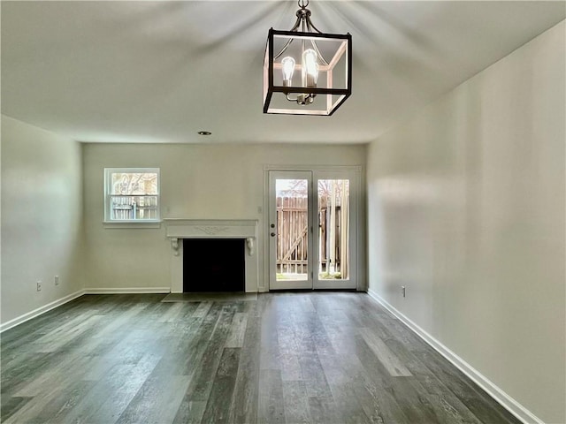 unfurnished living room featuring plenty of natural light, dark hardwood / wood-style floors, and an inviting chandelier