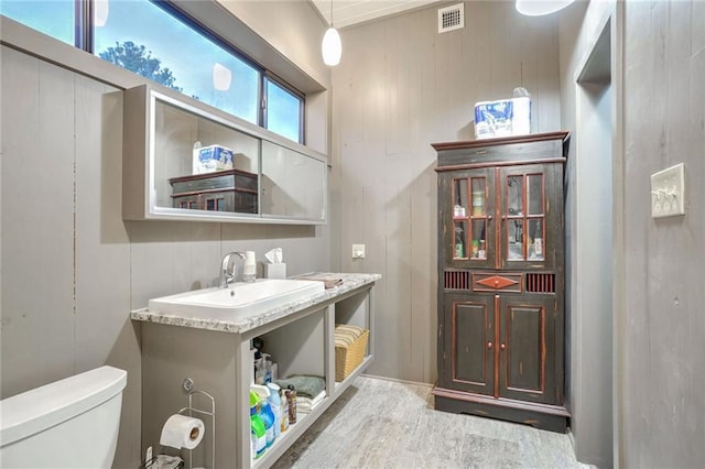 bathroom featuring toilet, wood walls, a sink, and visible vents
