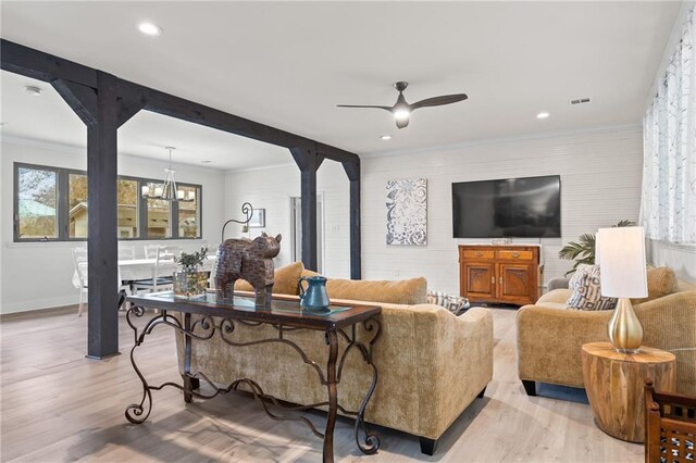 living room with ceiling fan with notable chandelier, ornamental molding, and light hardwood / wood-style floors