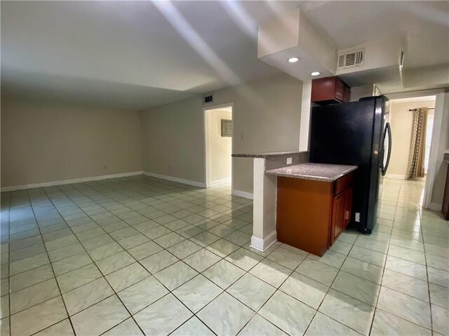 kitchen with black refrigerator, light tile patterned floors, light stone countertops, and kitchen peninsula