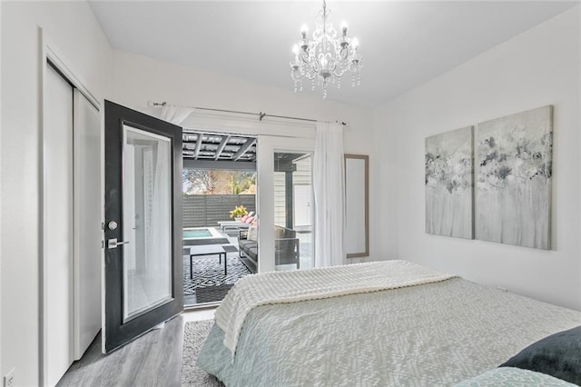 bedroom featuring wood-type flooring, access to exterior, an inviting chandelier, and a closet