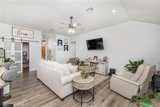 living room featuring ceiling fan, a barn door, lofted ceiling, and light hardwood / wood-style floors