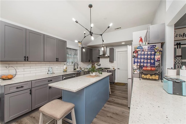 kitchen with gray cabinetry, wall chimney range hood, decorative light fixtures, and a kitchen bar