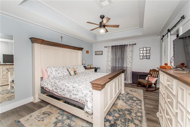 bedroom with ceiling fan, dark hardwood / wood-style flooring, a barn door, and a raised ceiling