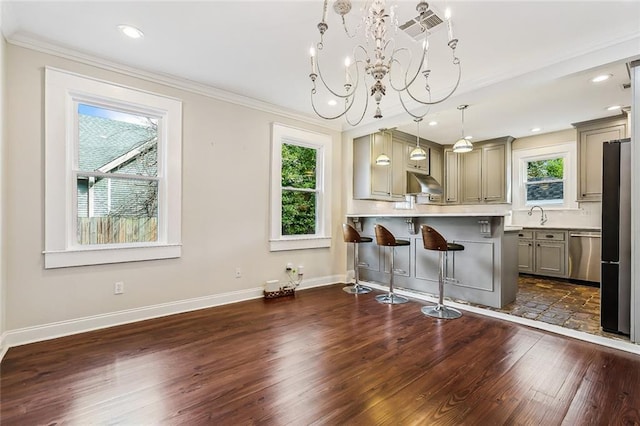 kitchen with a kitchen bar, decorative light fixtures, appliances with stainless steel finishes, dark hardwood / wood-style flooring, and ornamental molding