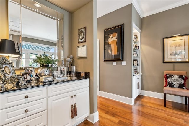 bar featuring sink, crown molding, white cabinetry, dark stone countertops, and light wood-type flooring