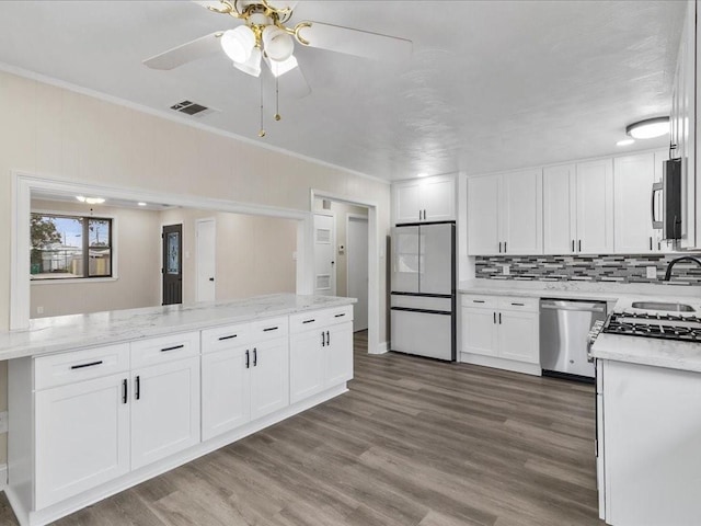 kitchen with crown molding, appliances with stainless steel finishes, white cabinets, hardwood / wood-style flooring, and backsplash