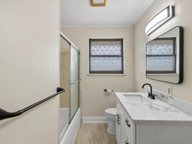 full bathroom with hardwood / wood-style flooring, bath / shower combo with glass door, vanity, ornamental molding, and toilet