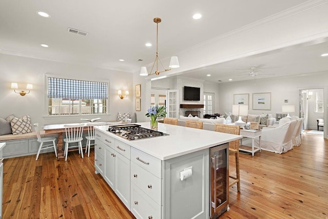 kitchen featuring white cabinetry, a center island, stainless steel gas cooktop, decorative light fixtures, and beverage cooler