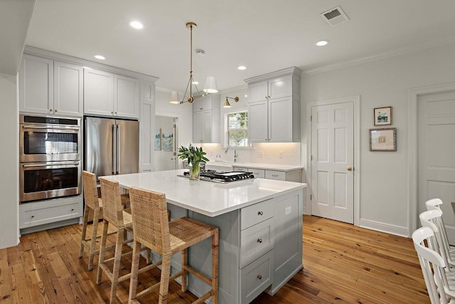 kitchen featuring pendant lighting, white cabinetry, stainless steel appliances, a center island, and ornamental molding