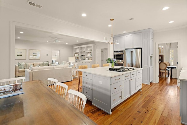 kitchen featuring a kitchen island, appliances with stainless steel finishes, decorative light fixtures, white cabinets, and crown molding