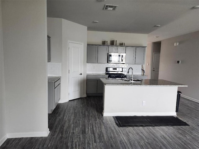 kitchen with sink, gray cabinets, appliances with stainless steel finishes, dark hardwood / wood-style floors, and an island with sink