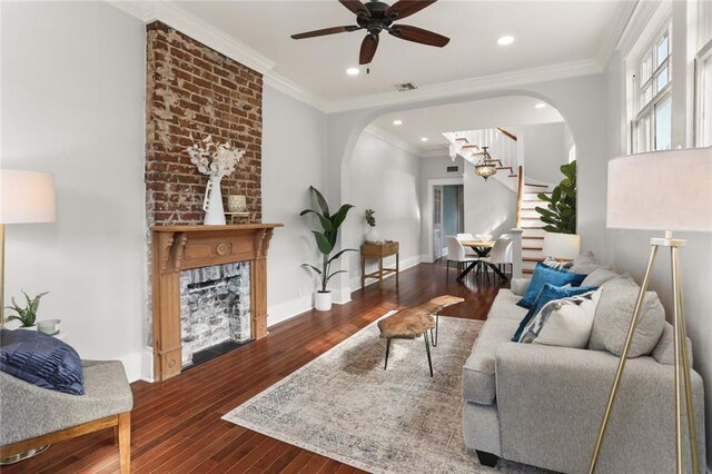 living room with a brick fireplace, wood-type flooring, ornamental molding, and ceiling fan