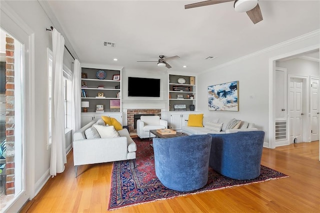 living room with hardwood / wood-style floors, built in features, ceiling fan, crown molding, and a brick fireplace