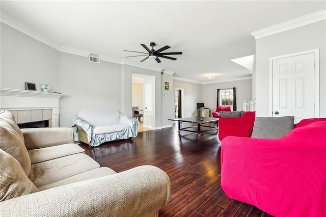 living room with dark wood-type flooring, ceiling fan, crown molding, and a tile fireplace