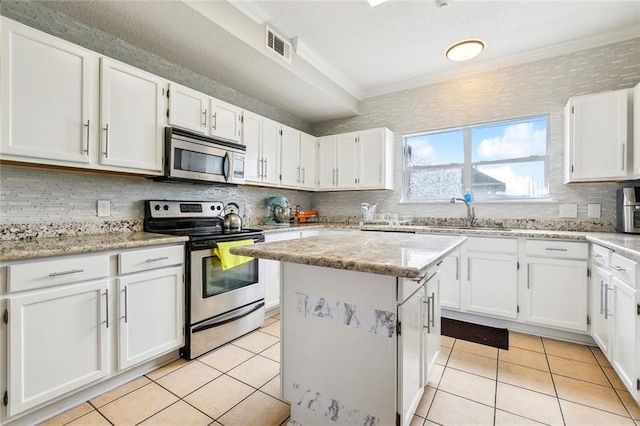 kitchen featuring light tile patterned flooring, a kitchen island, white cabinets, stainless steel appliances, and light stone countertops