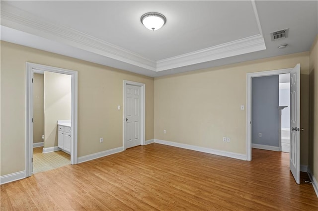 unfurnished bedroom featuring ensuite bath, ornamental molding, light hardwood / wood-style floors, and a raised ceiling